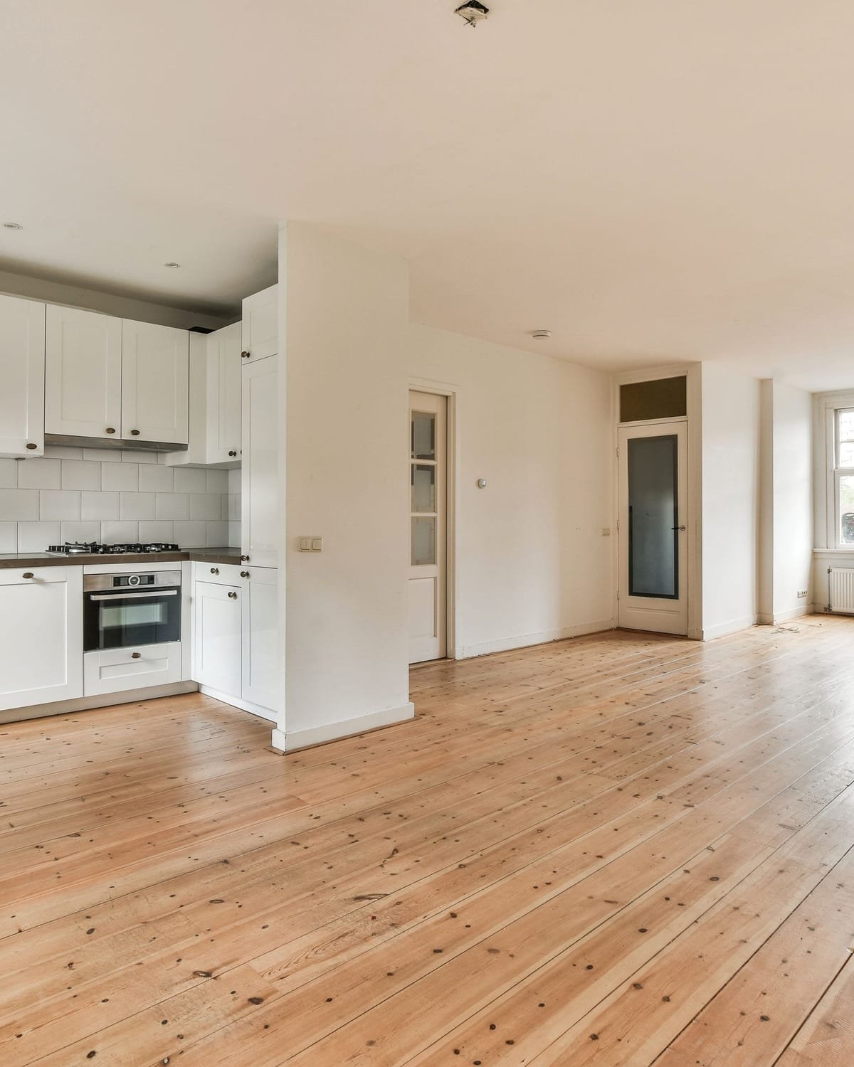 Interior de vivienda con cocina blanca instalada, puertas interiores de madera y suelo de tarima — los tres oficios de HTM en una misma estancia