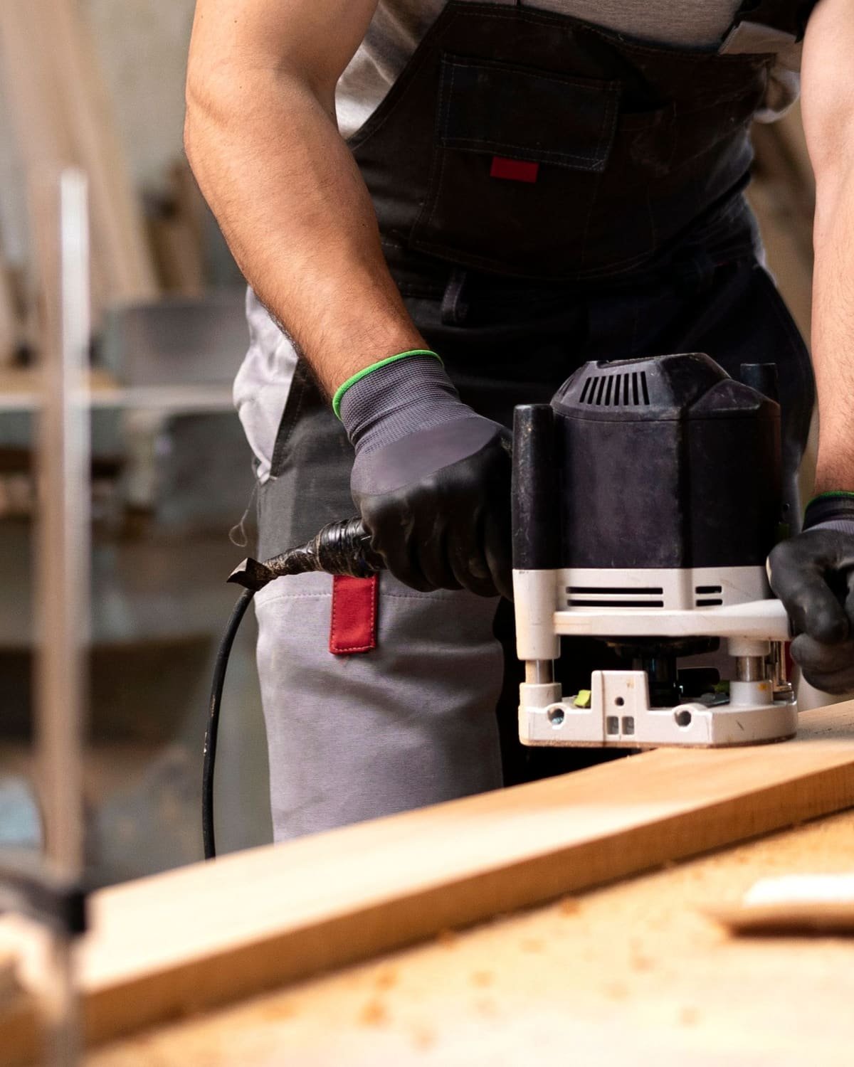 Instalador operando una fresadora sobre tablero de madera con mandil y guantes de trabajo